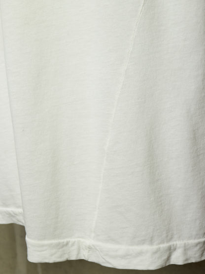 Close-up detail of a white cotton garment, showing the hem with a folded cuff and a diagonal seam running down the center.