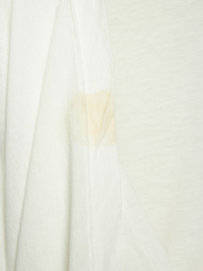A close-up of a white textured fabric, likely a t-shirt or jersey, showing a light beige stain or discoloration on the left side seam.