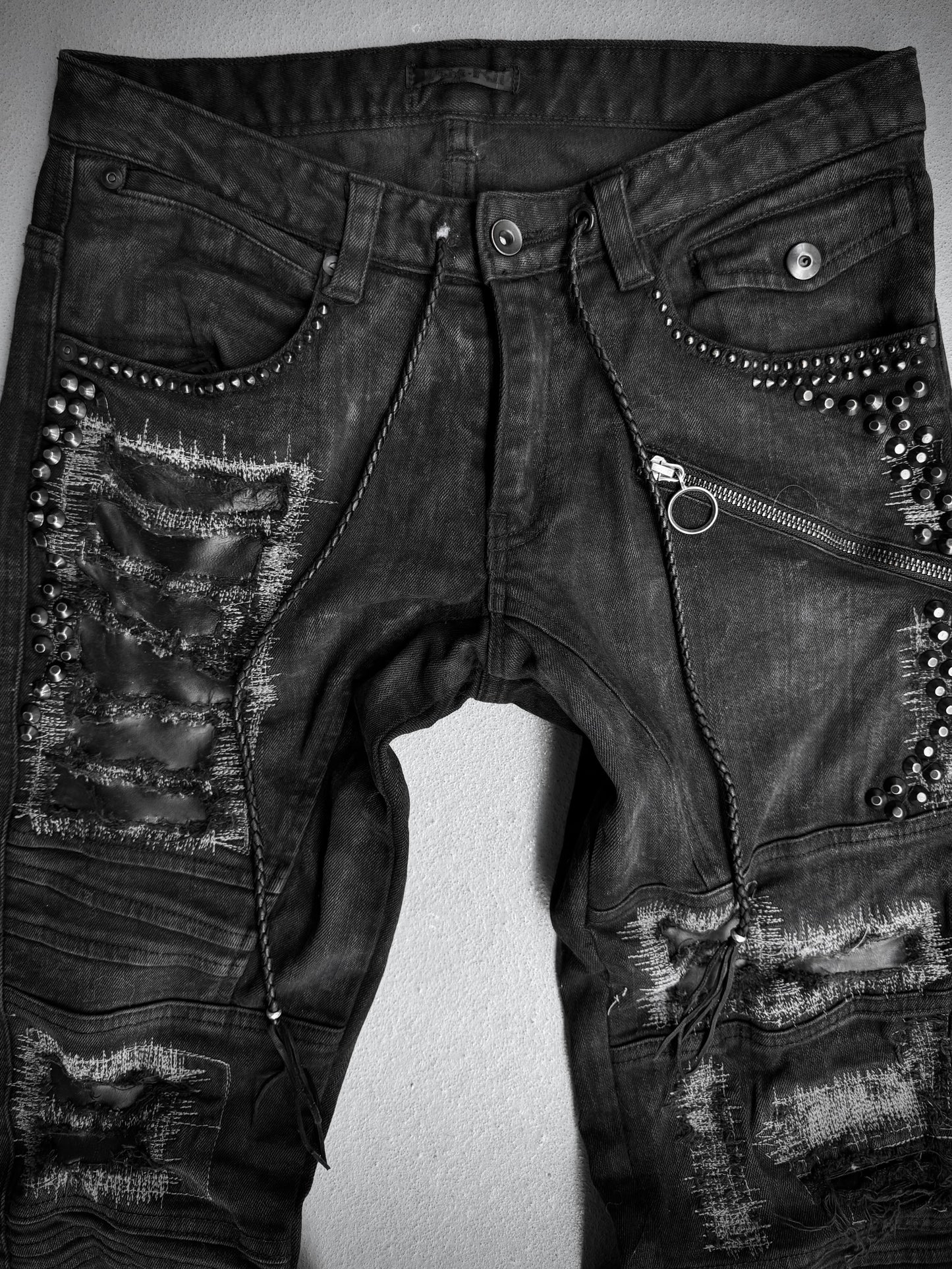 KMRii Early 00s Goatskin Patches Studded Crush Flare-zip Denim—black jeans featuring distressed details, fading, metal studs, horizontal zipper above one pocket, frayed patches, and decorative stitching. Size 2 (US 29-30 waist).