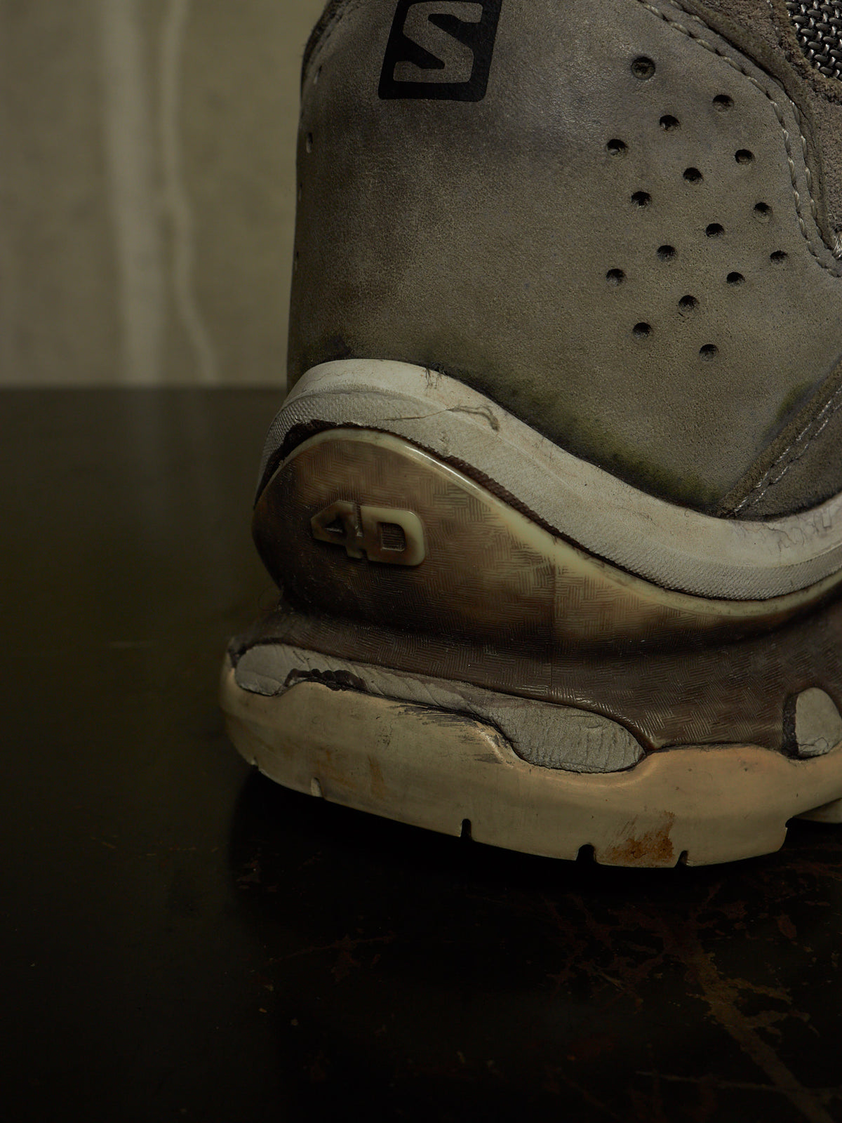 Close-up of the heel and midsole of a worn gray Salomon sneaker, showing visible dirt, scuffing, and a black Salomon logo near the top.
