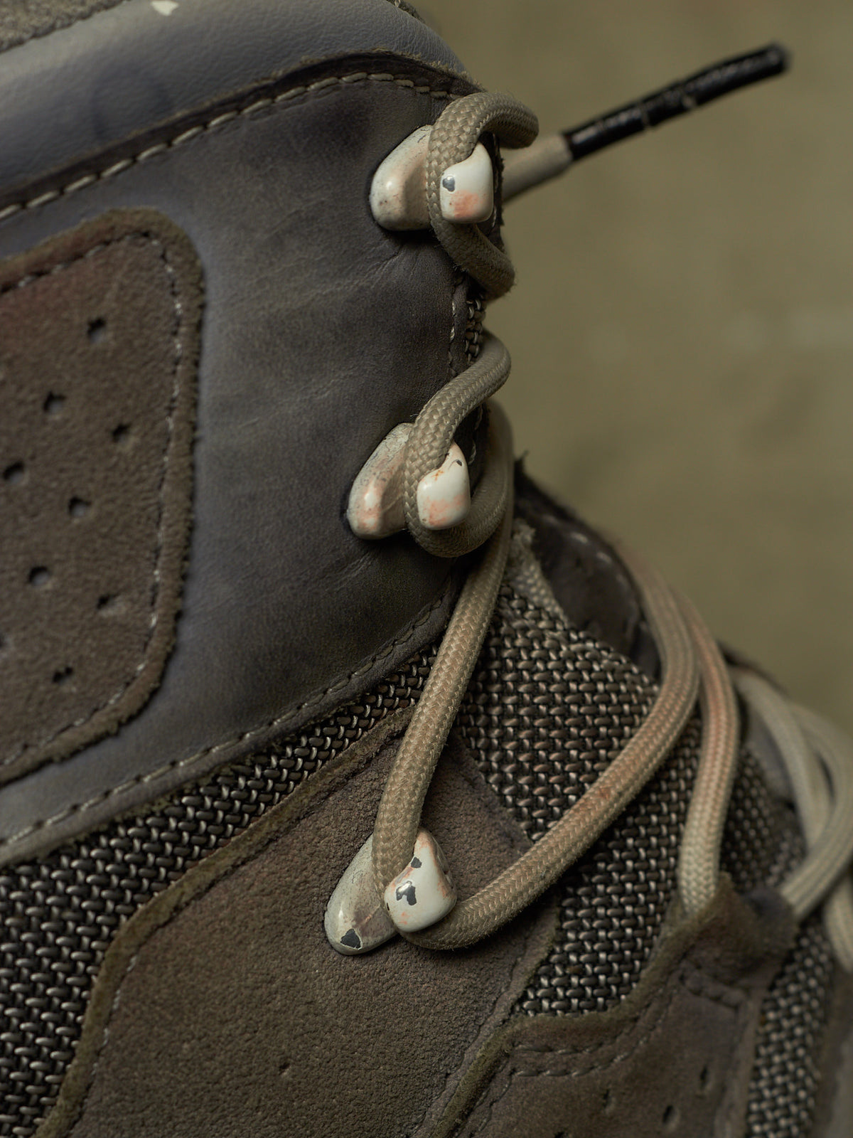 Close-up of a brown and gray high-top lace-up boot with beige laces threaded through metal eyelets.