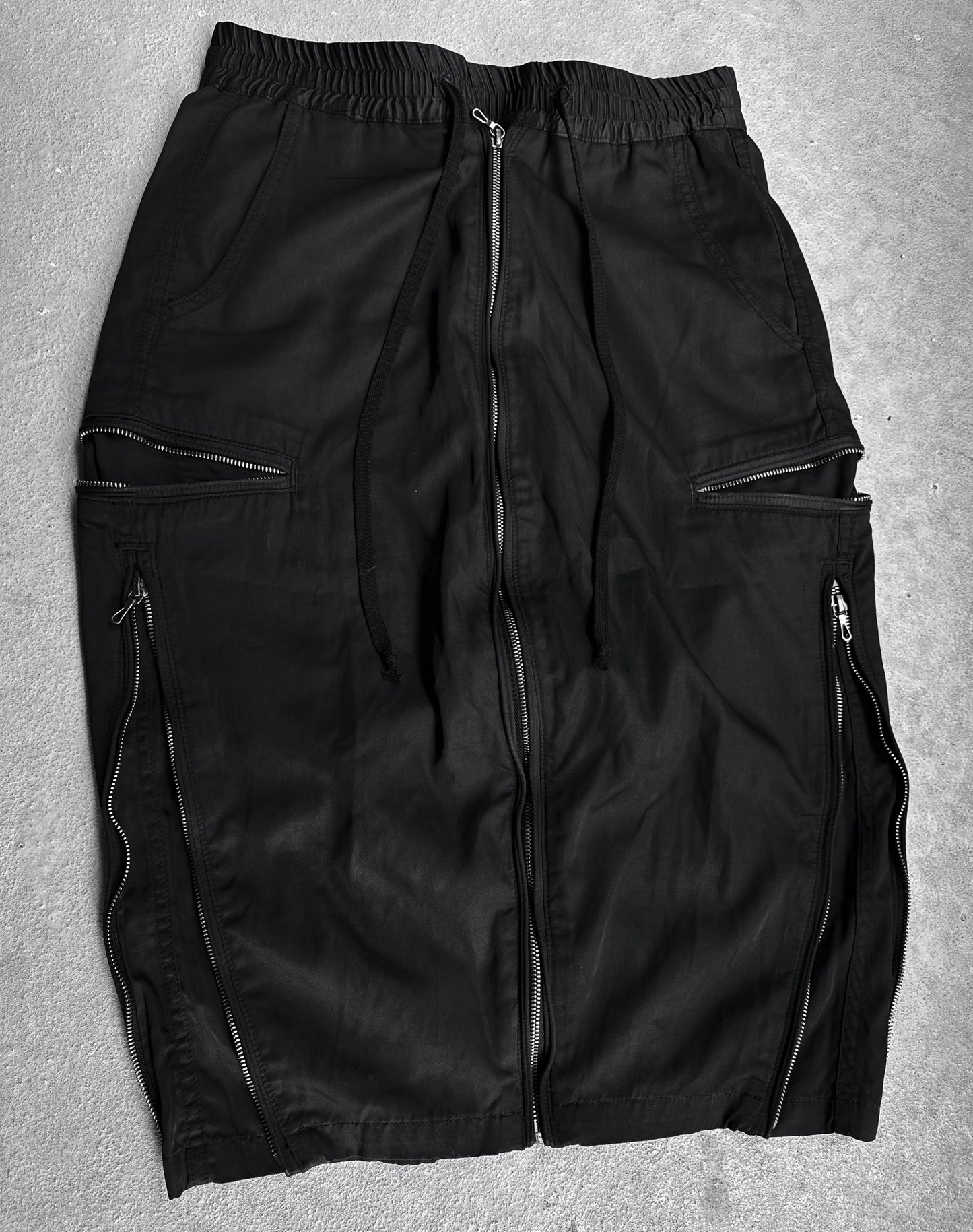 The DRIEW Julius_7 SS10 “neurbanvolker;” Convertible Multi-zip Cotton Twill Shorts, black with elastic waistband, drawstring, and multiple visible zippers. Fits US 29-32 waist; flawless condition. Laid flat on a light textured surface.