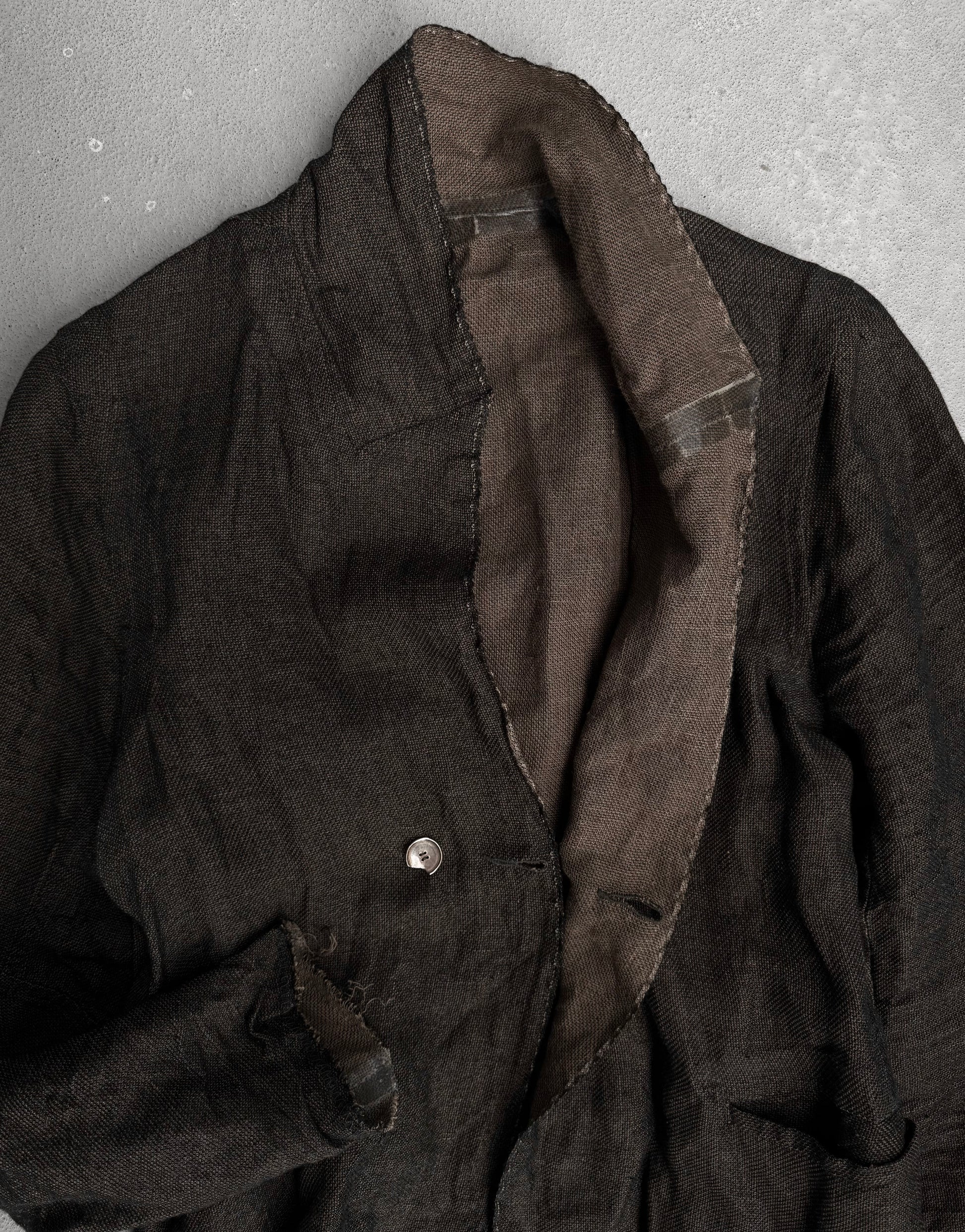 The TaichiMurakami “Coin” Taped Seam Collarless Work Blazer features dark textured Japanese linen, a single visible button, and contrasting brown lining. Its slightly worn look is inspired by industrial minimalism.