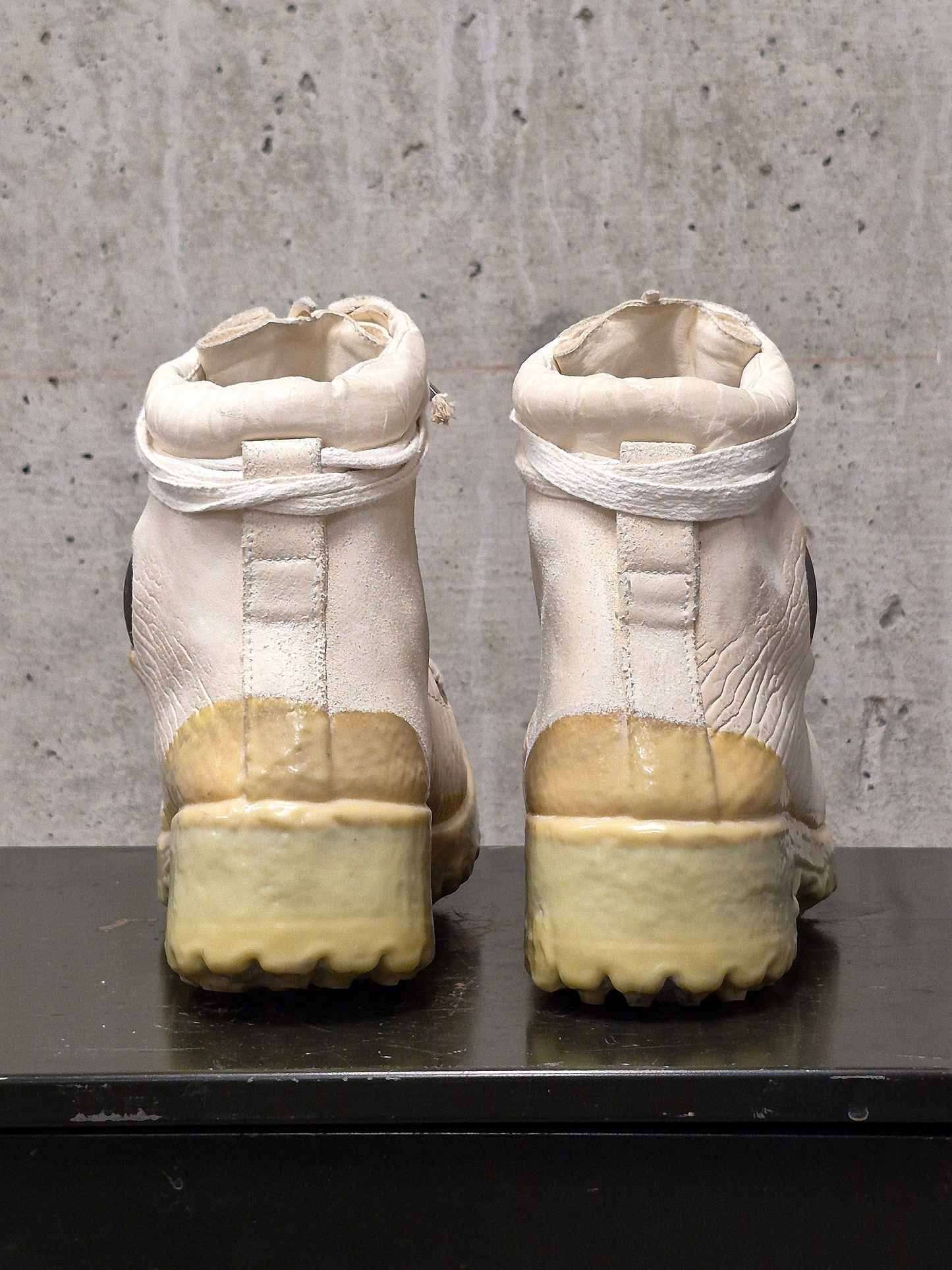 Pair of white boots with yellow soles on a gray surface