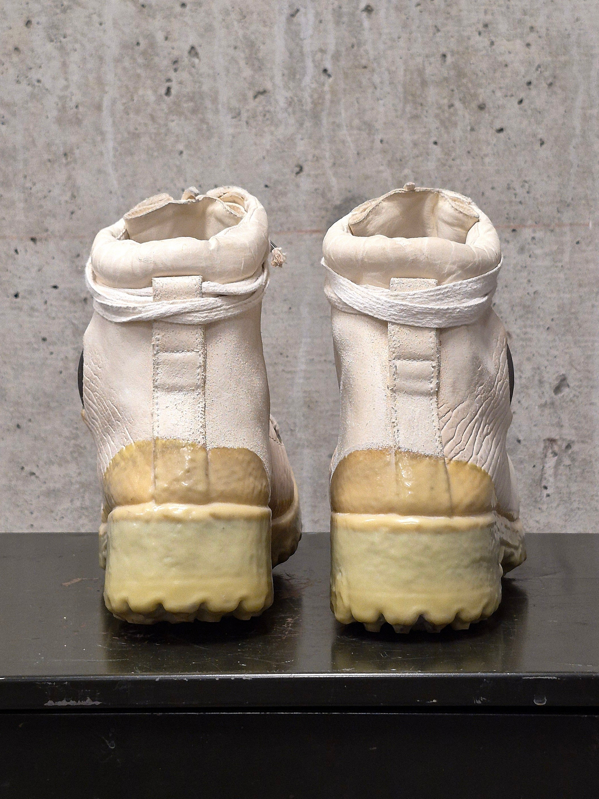 Pair of white boots with yellow soles on a gray surface