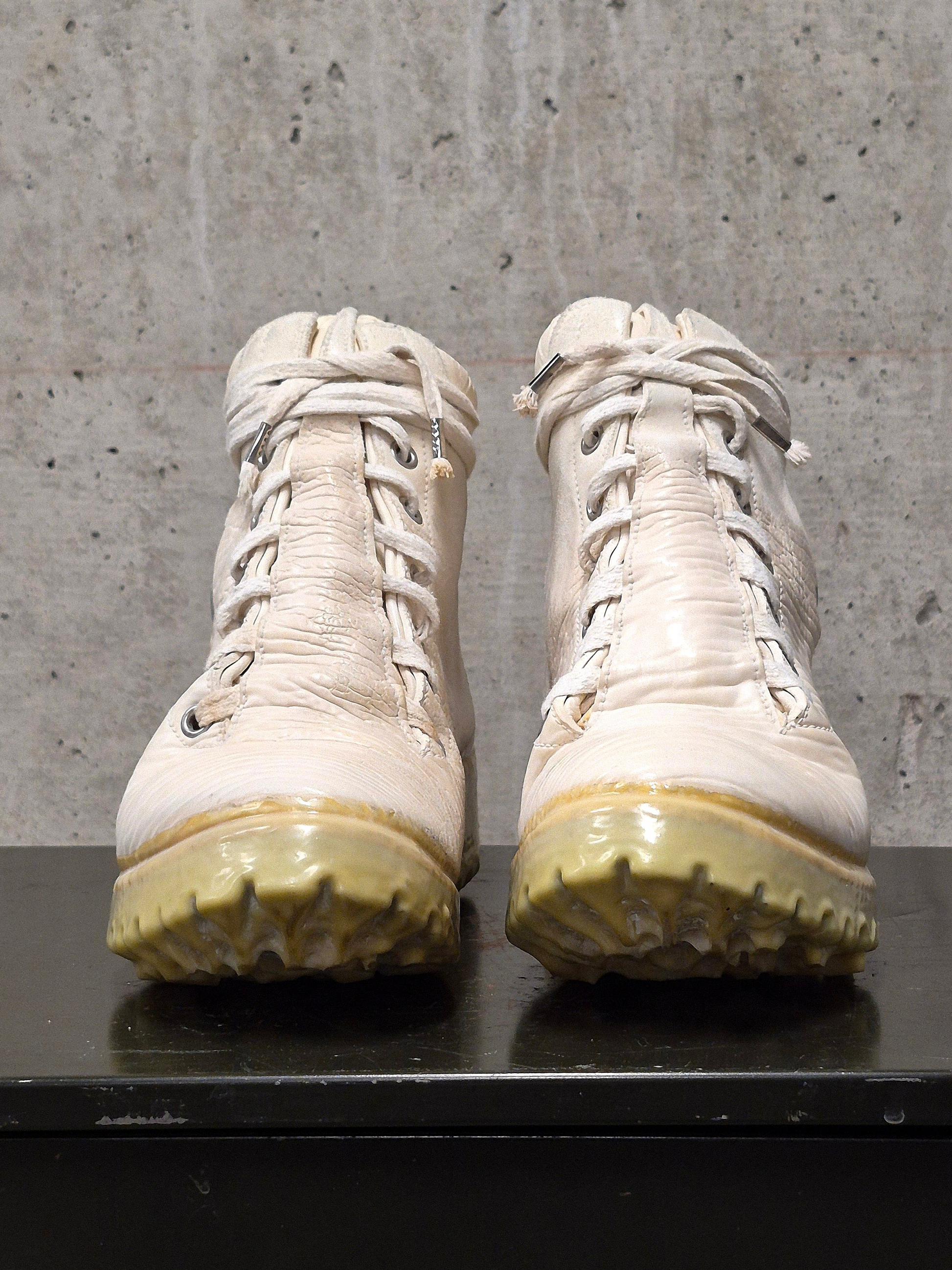 Pair of white boots with yellowed soles on a concrete floor.