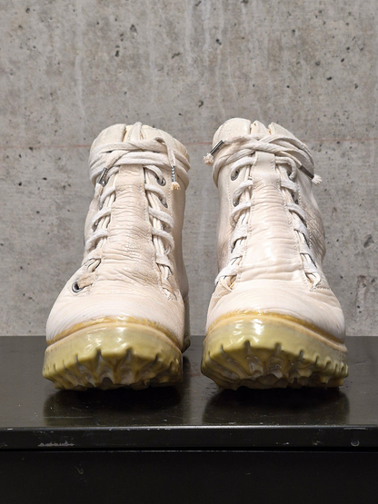 Pair of white boots with yellowed soles on a concrete floor.