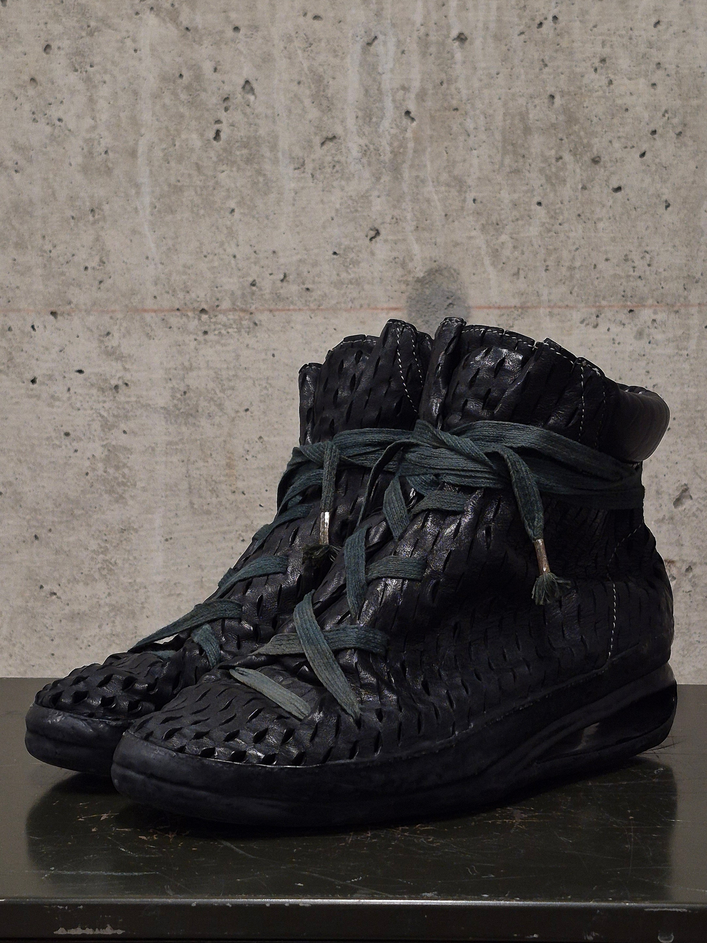Black high-top sneakers with textured design on a concrete surface