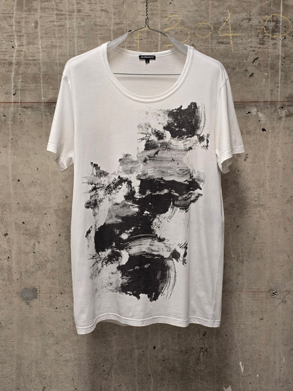 White t-shirt with black abstract design on a hanger against a textured wall.