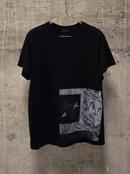 Black t-shirt with a graphic design on a hanger against a textured wall.
