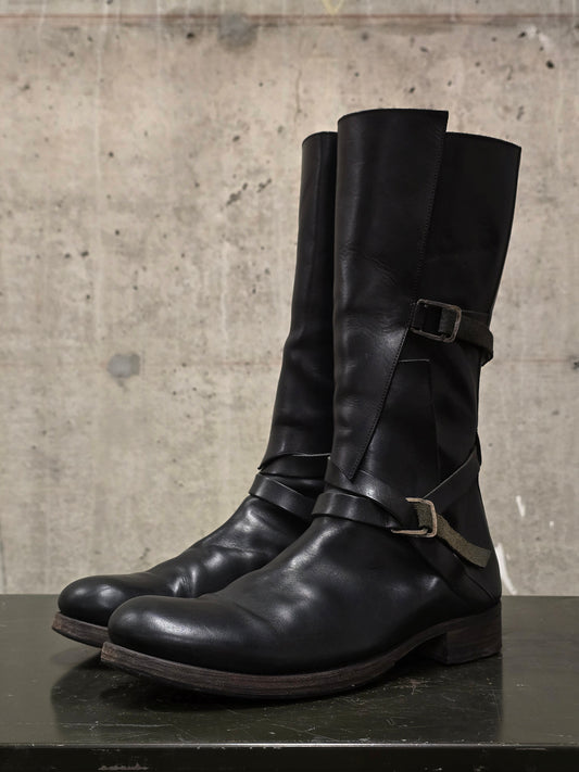 Pair of black leather boots with buckles on a concrete surface