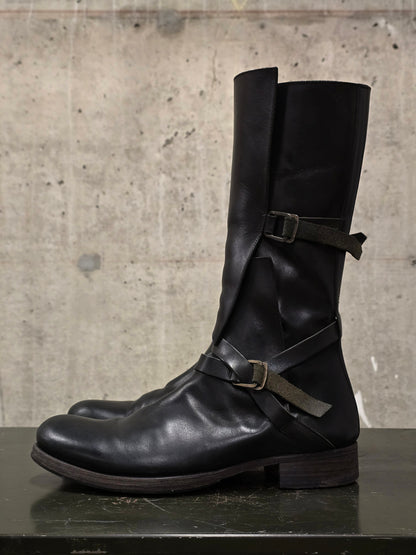 Black leather boots with buckles on a concrete surface
