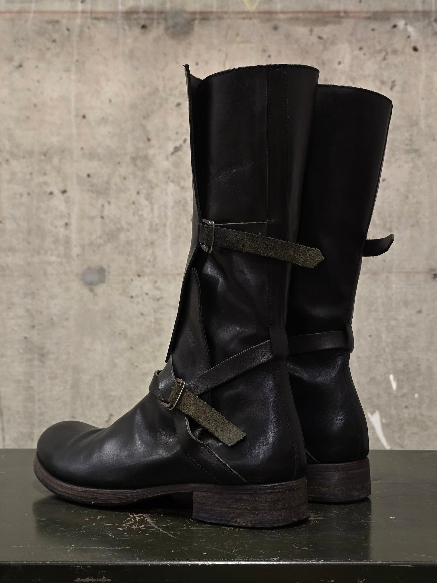 Black leather boots with buckles on a textured surface