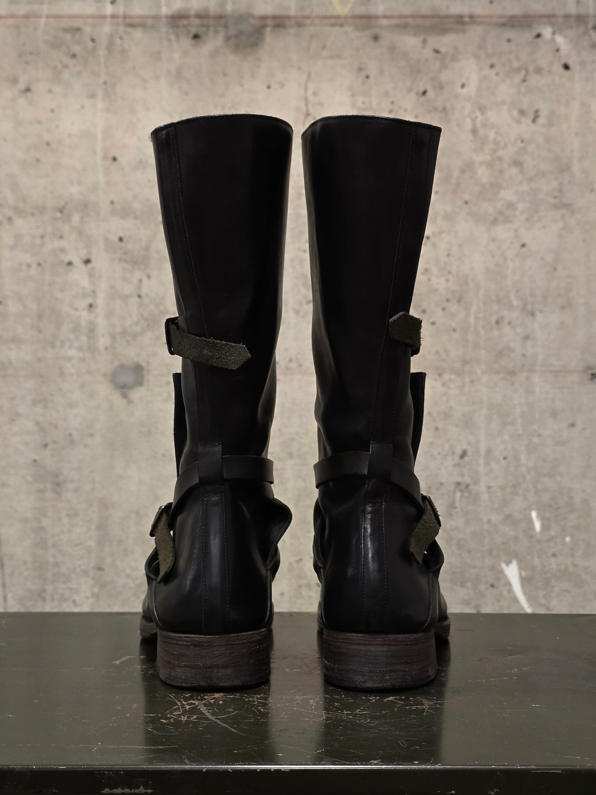 Pair of black leather boots with buckles on a concrete surface