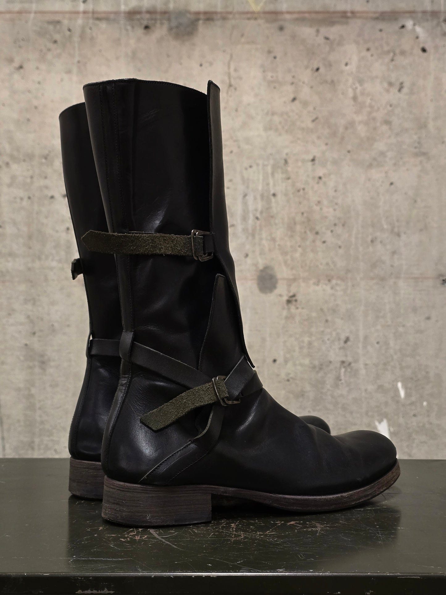 Pair of black leather boots with buckles on a concrete surface