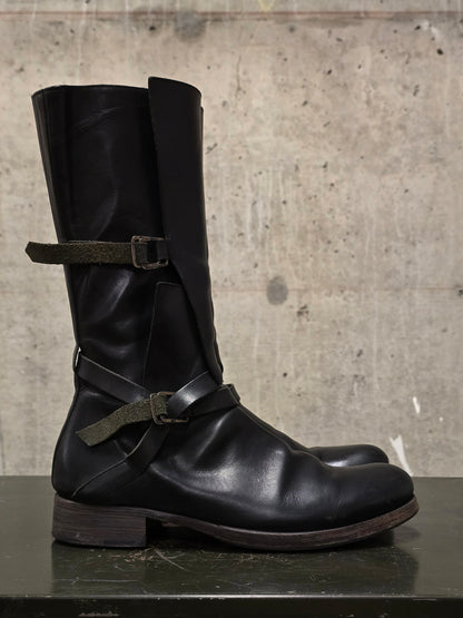 Black leather boot with straps on a concrete surface