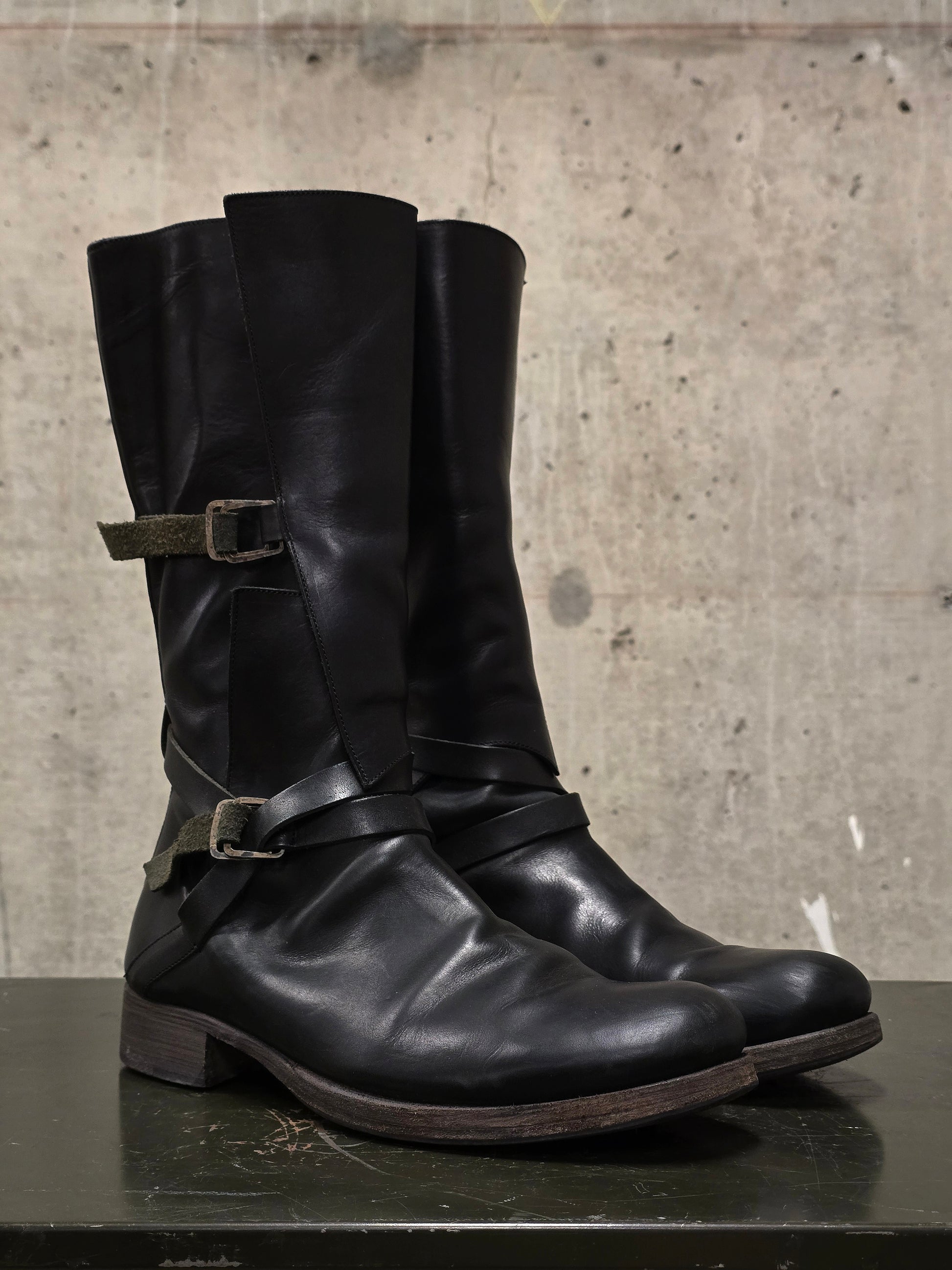 Pair of black leather boots with buckles on a concrete surface