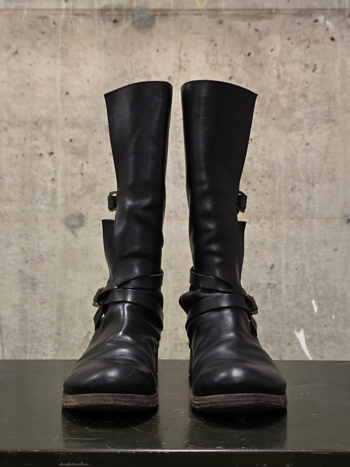 Pair of black leather boots with buckles on a concrete surface
