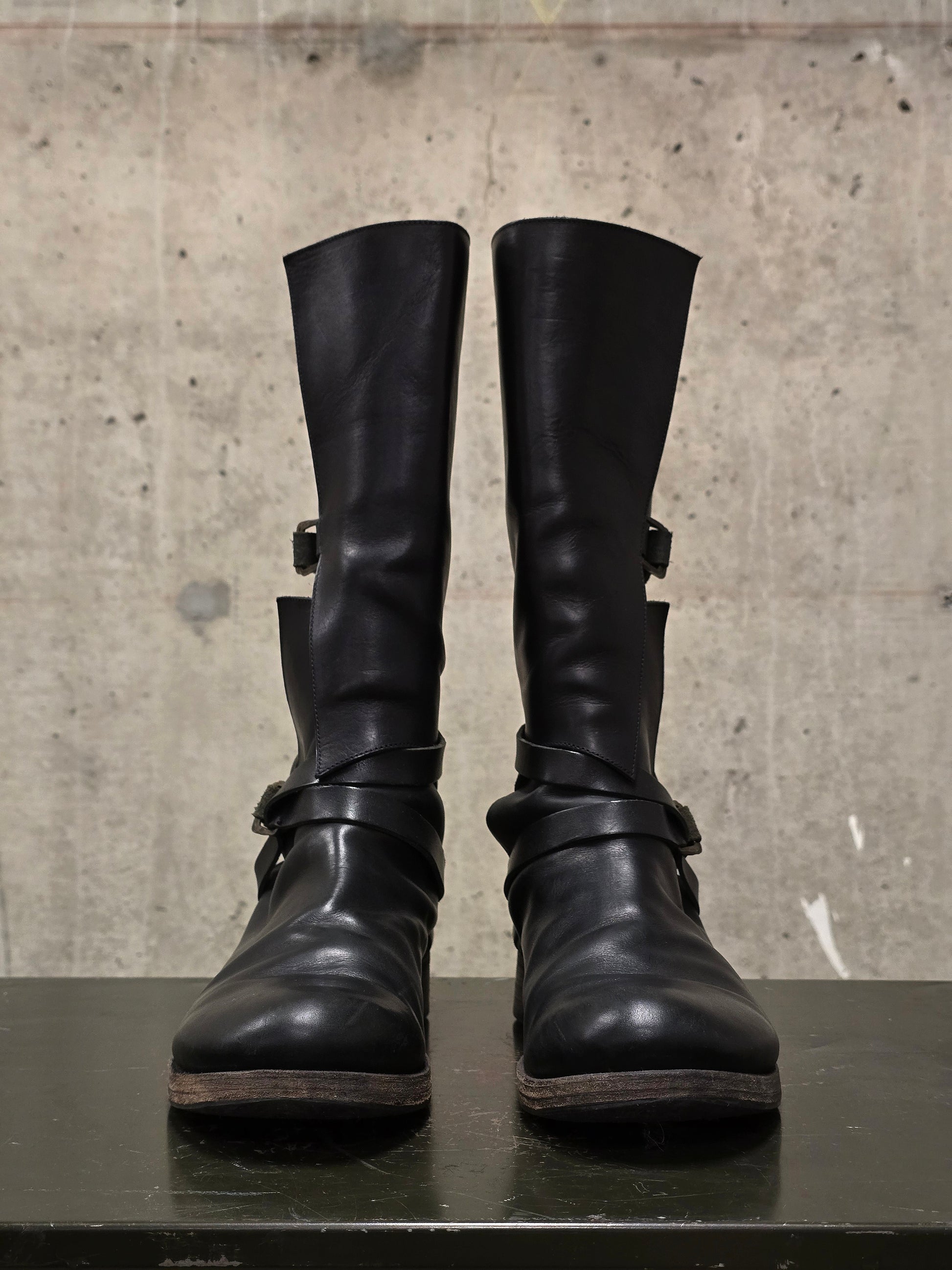 Pair of black leather boots with buckles on a concrete surface