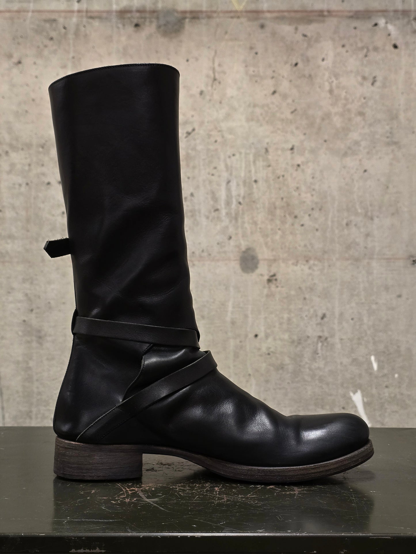 Black leather boot with straps on a concrete surface