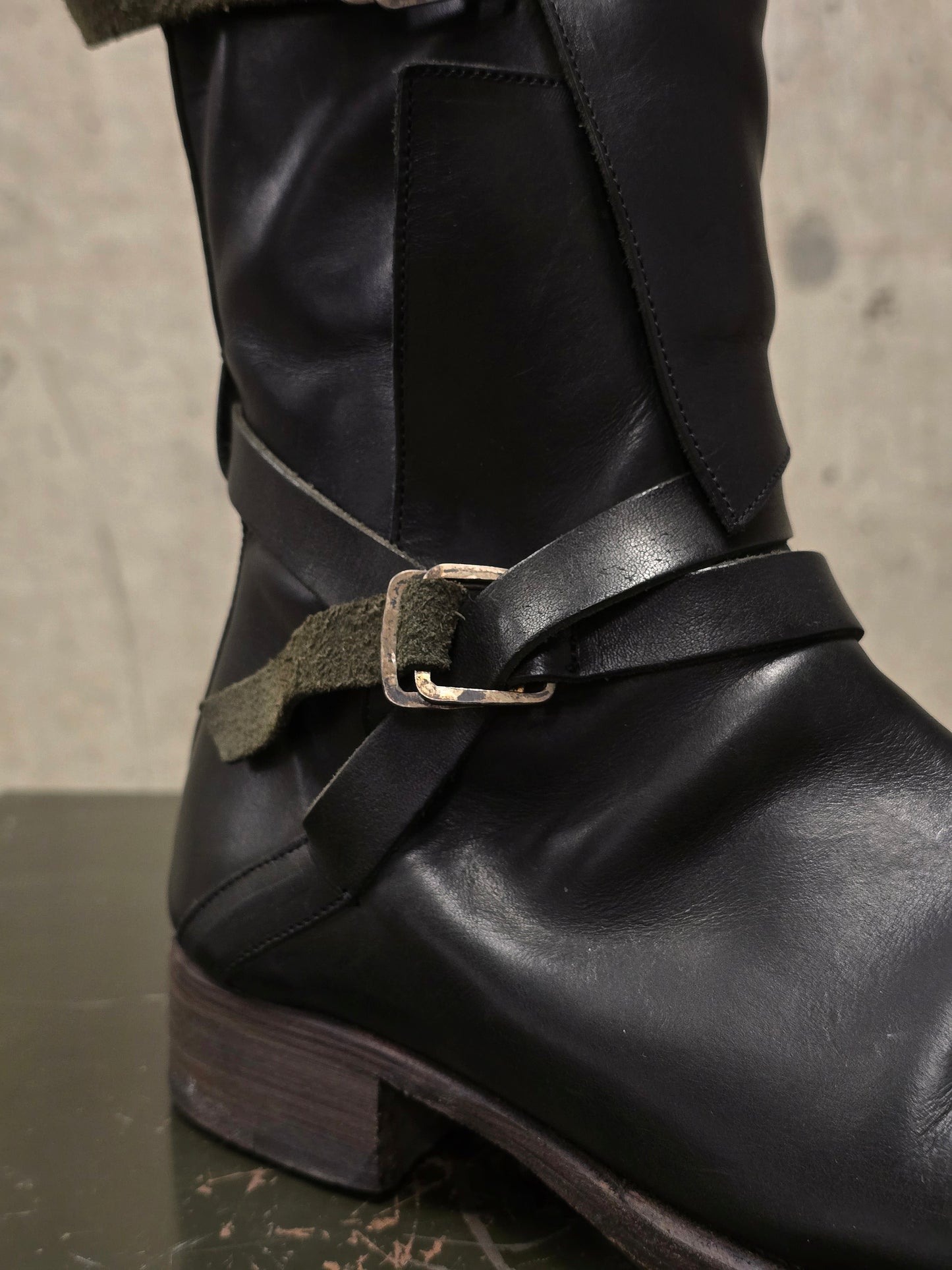 Black leather boot with a buckle on a neutral background
