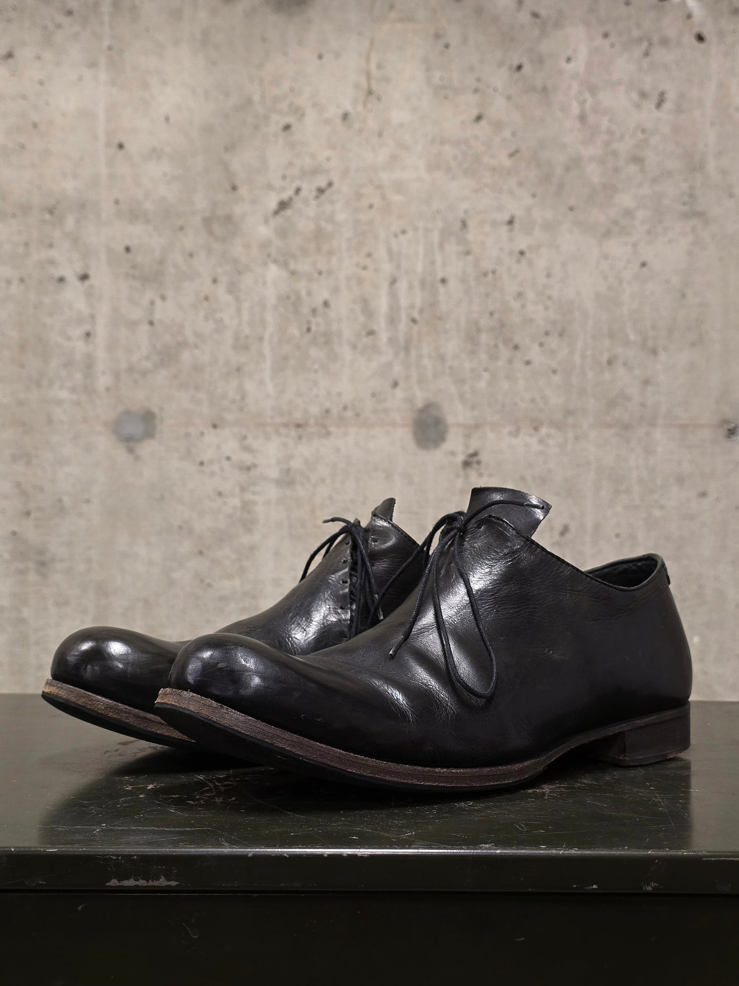 Pair of black leather shoes on a dark surface with a concrete wall background