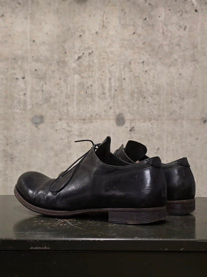 Pair of black leather shoes on a dark surface with a concrete wall background