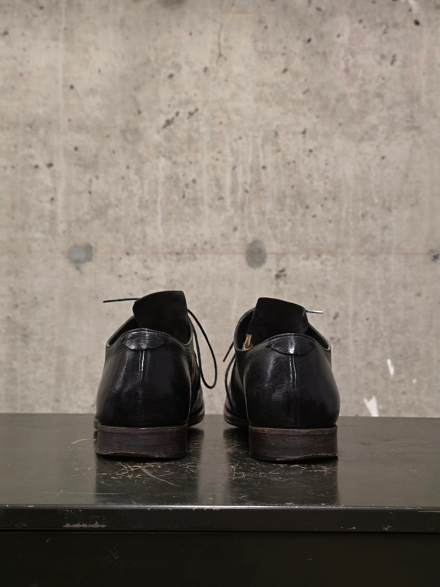 Pair of black leather shoes on a dark surface with a concrete wall background
