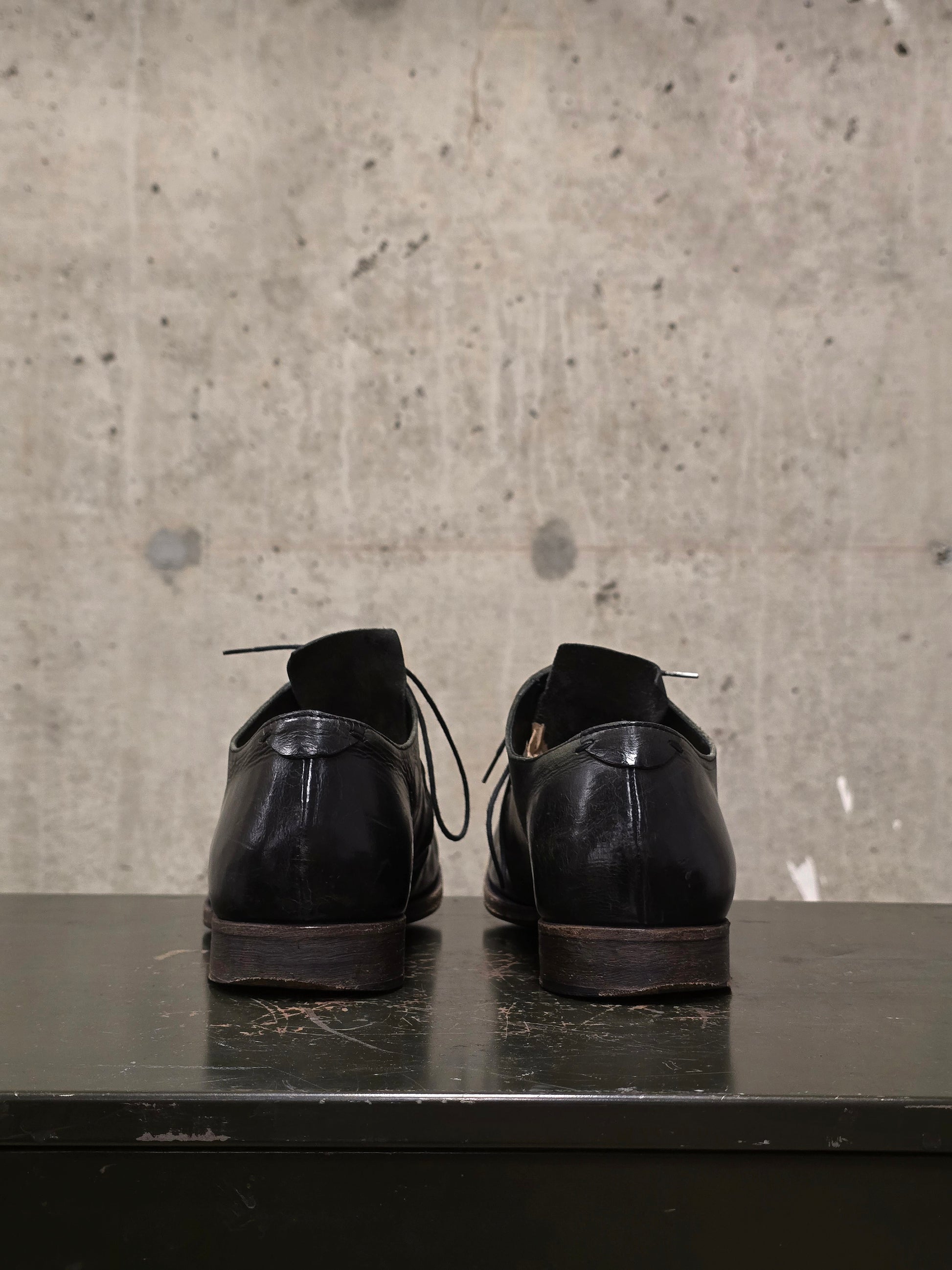 Pair of black leather shoes on a dark surface with a concrete wall background