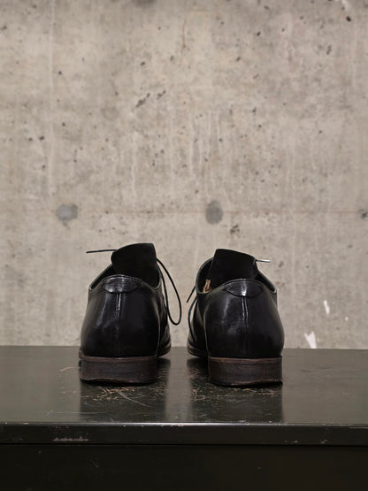 Pair of black leather shoes on a dark surface with a concrete wall background