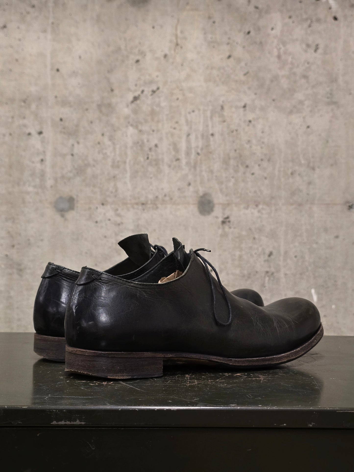 Pair of black leather shoes on a dark surface with a concrete wall background