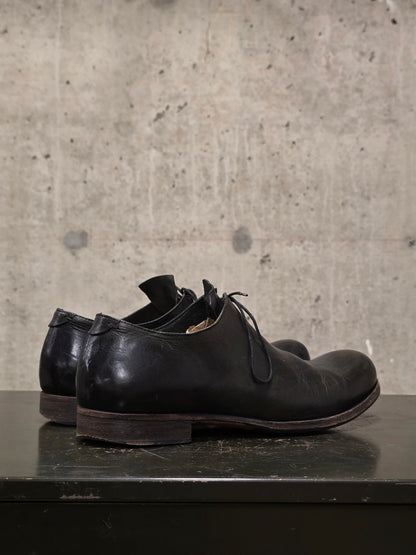 Pair of black leather shoes on a dark surface with a concrete wall background