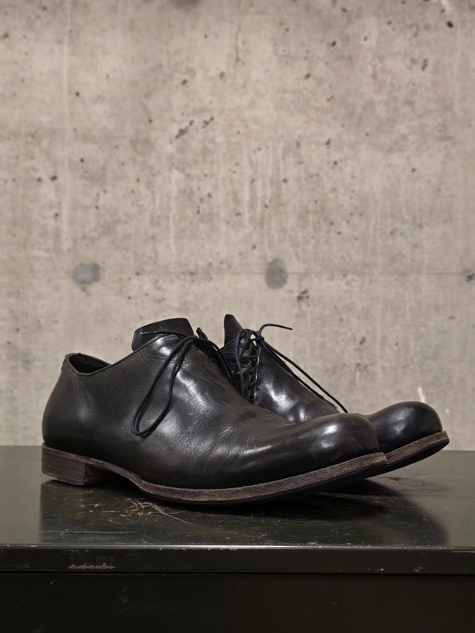 Pair of black leather shoes on a dark surface with a concrete wall background