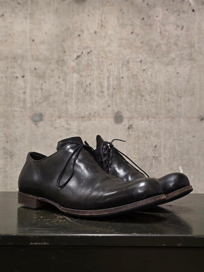 Pair of black leather shoes on a dark surface with a concrete wall background