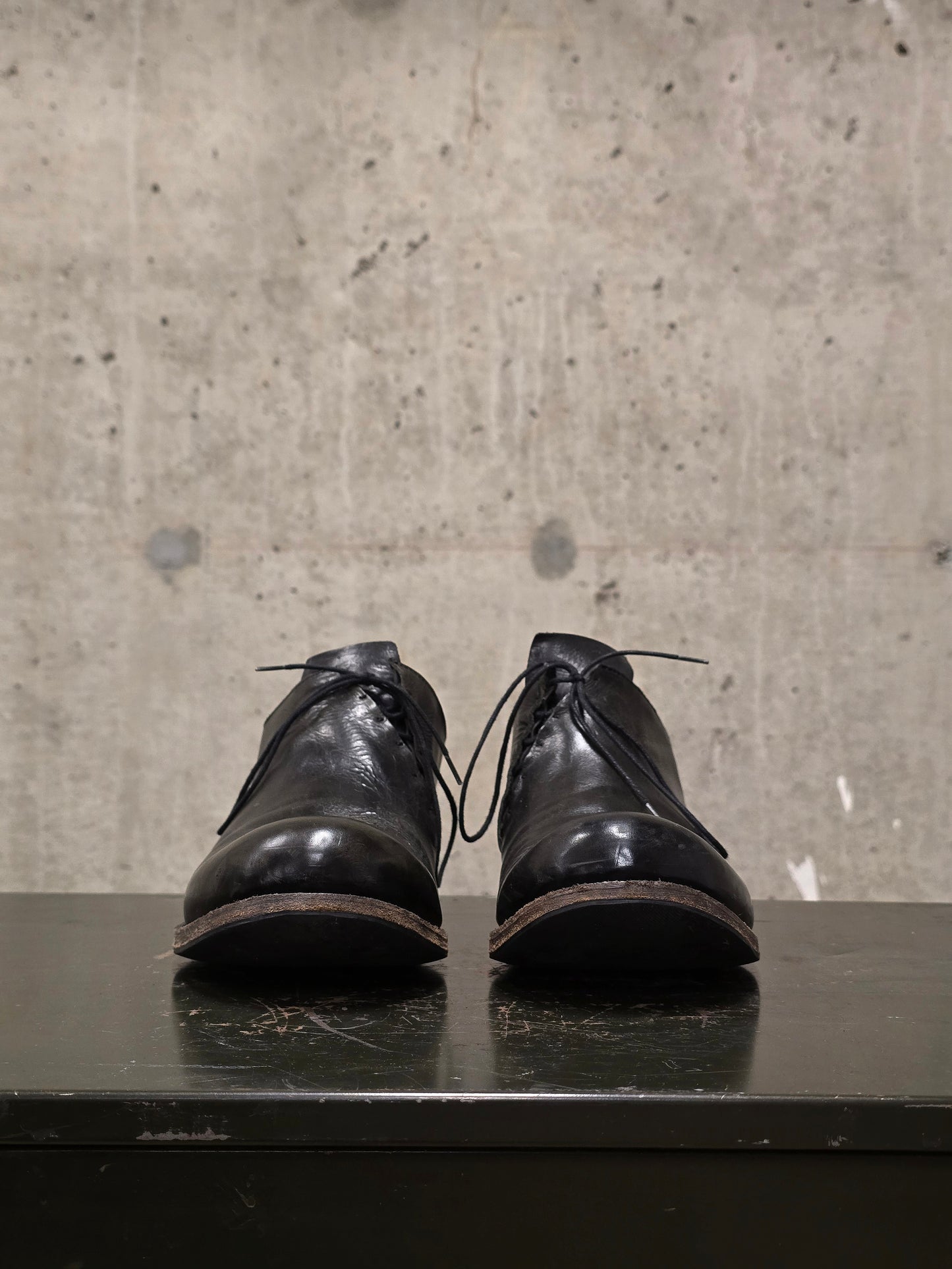 Pair of black leather shoes on a reflective surface with a concrete wall background
