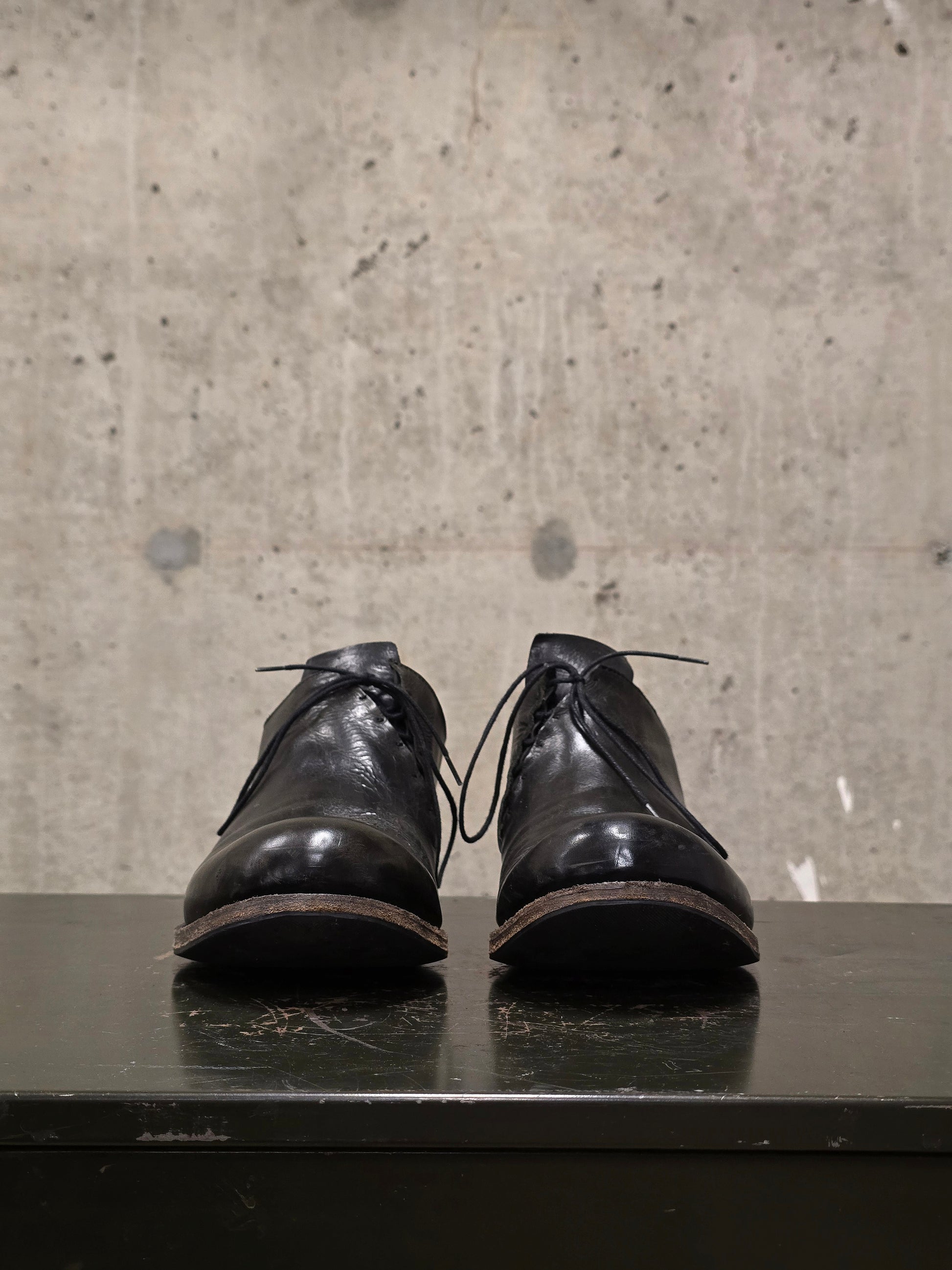 Pair of black leather shoes on a reflective surface with a concrete wall background