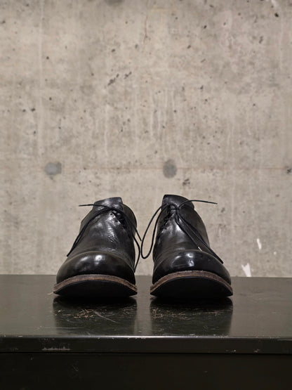 Pair of black leather shoes on a reflective surface with a concrete wall background