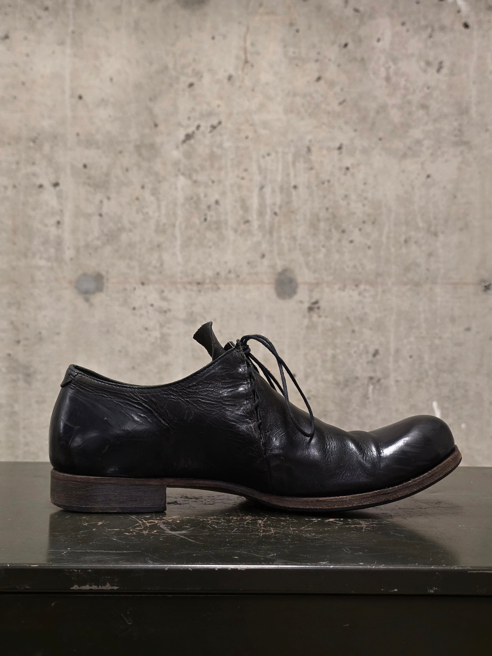Black leather shoe on a dark surface with a concrete wall background