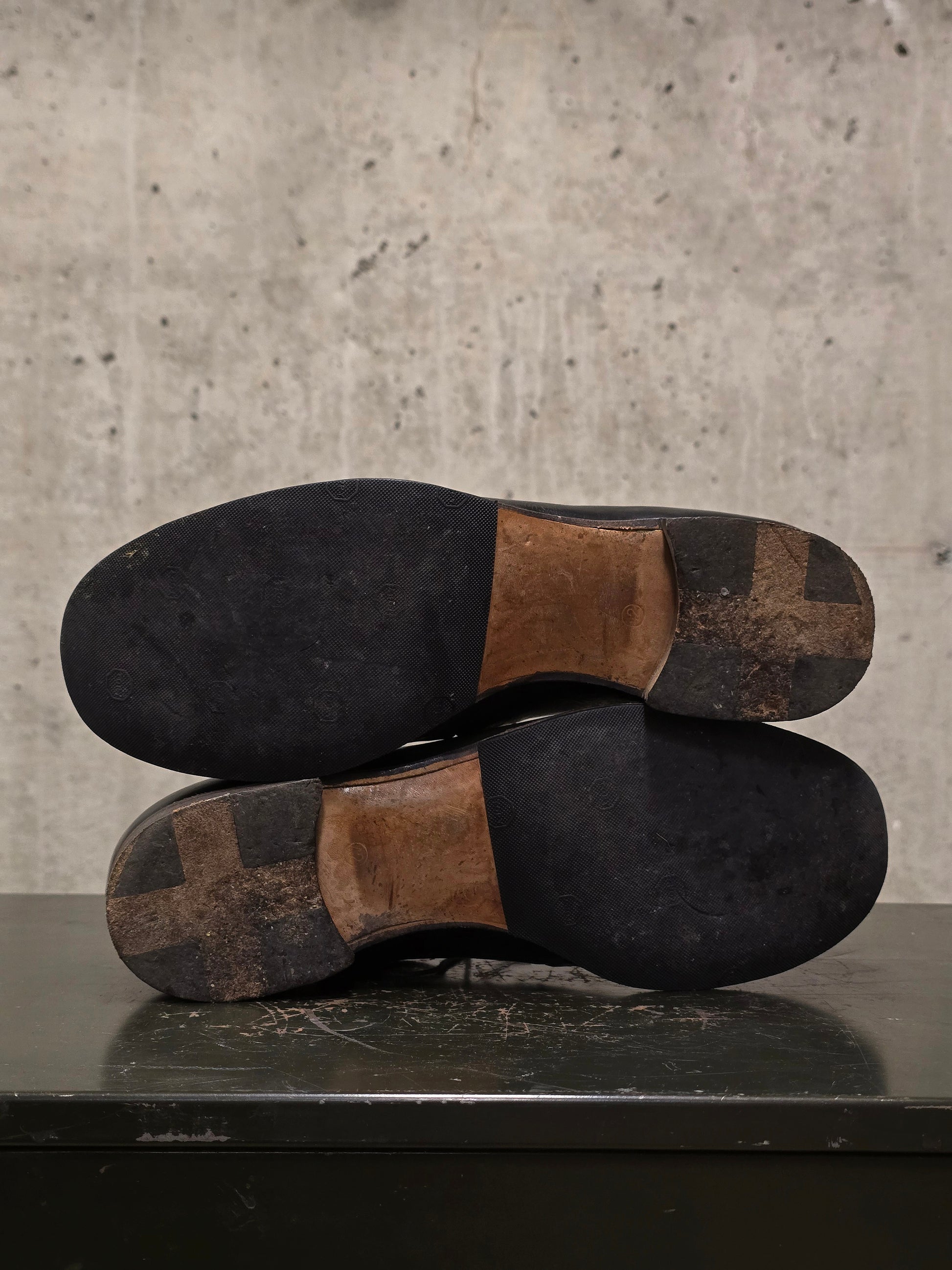 Pair of worn shoes with brown soles on a concrete surface
