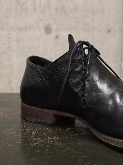 Black leather shoe with laces on a textured surface