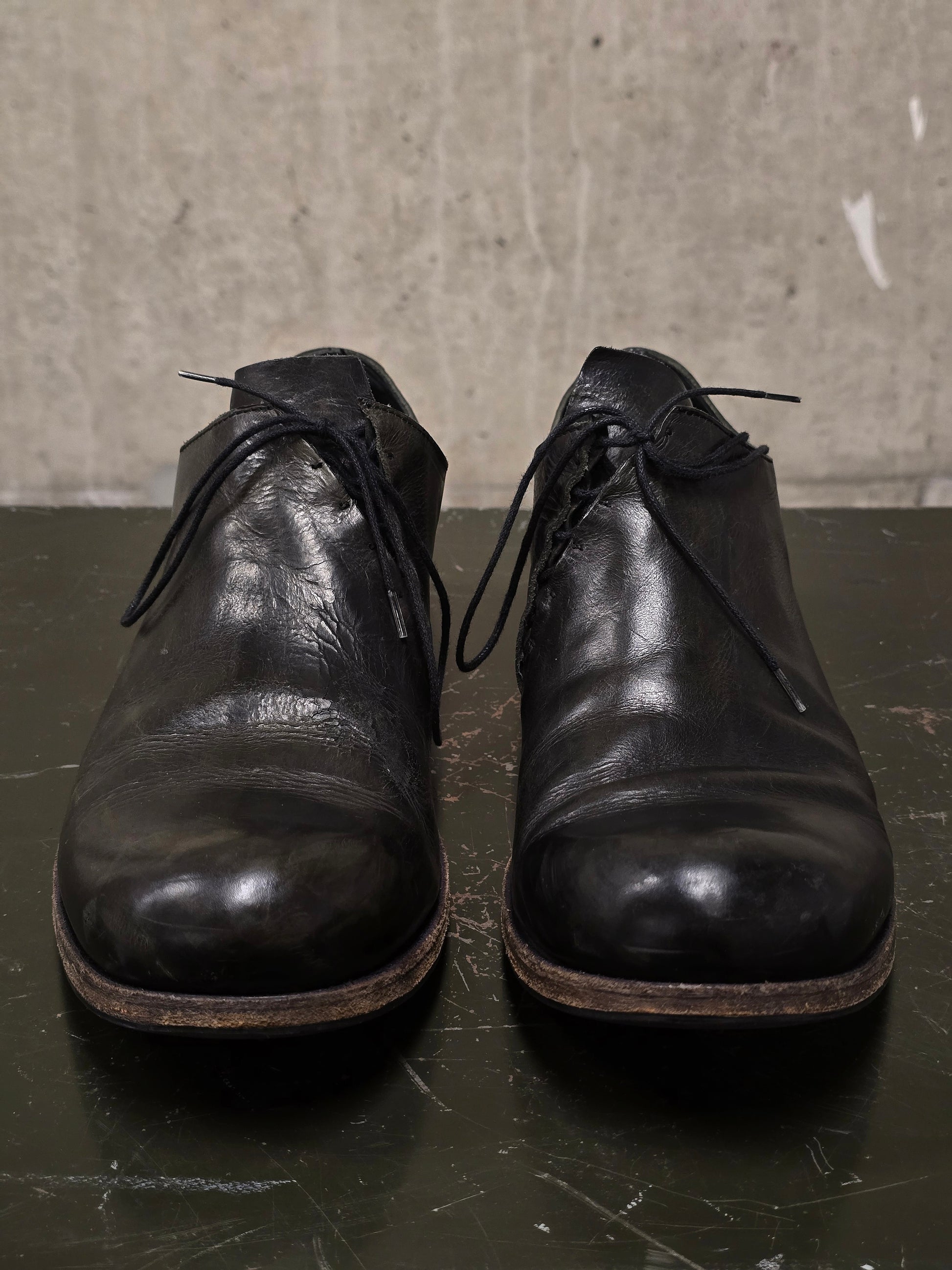 Pair of black leather shoes on a dark surface with a textured gray background