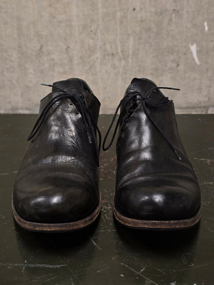 Pair of black leather shoes on a dark surface with a textured gray background