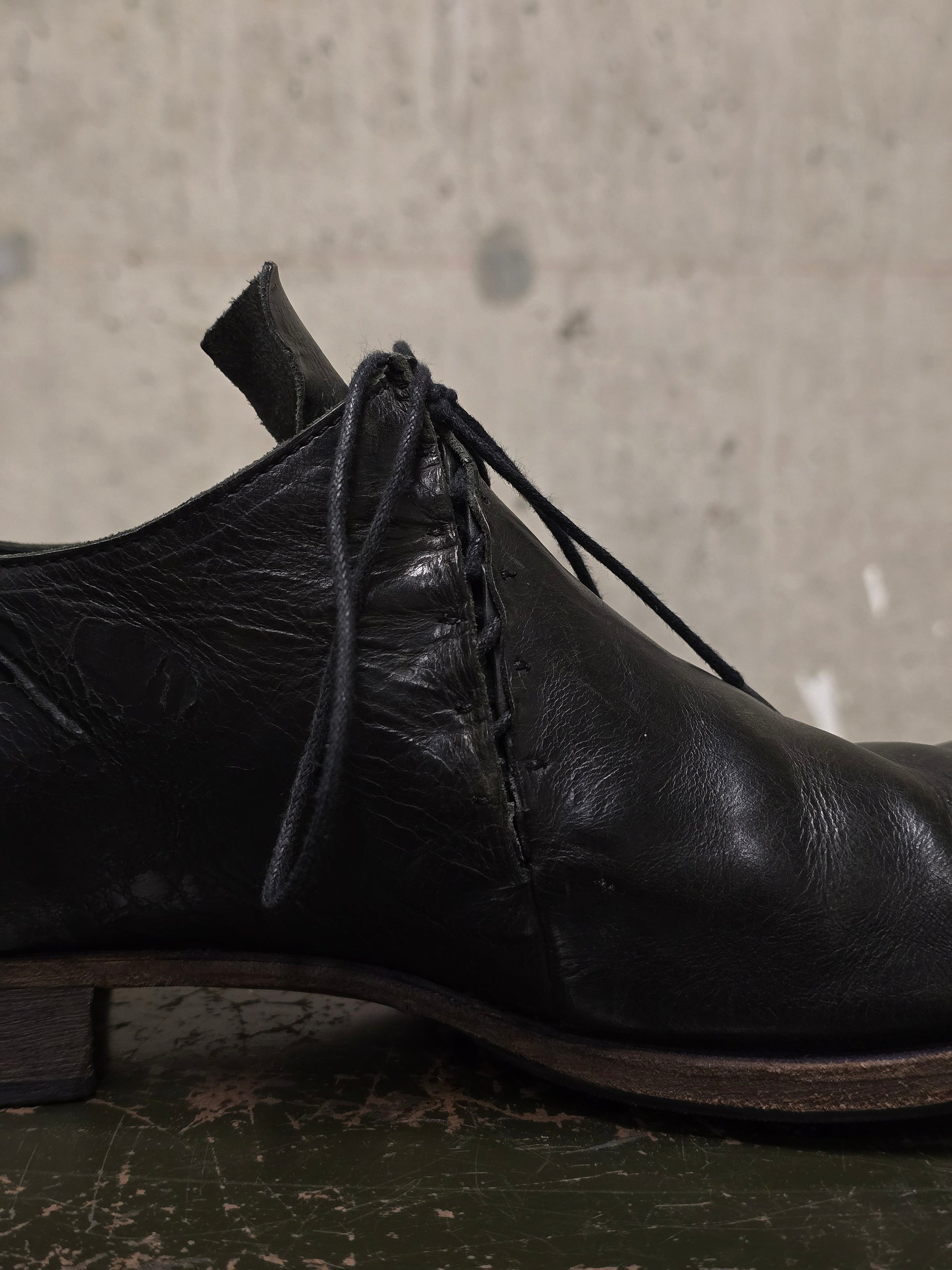 Black leather shoe with laces on a textured surface