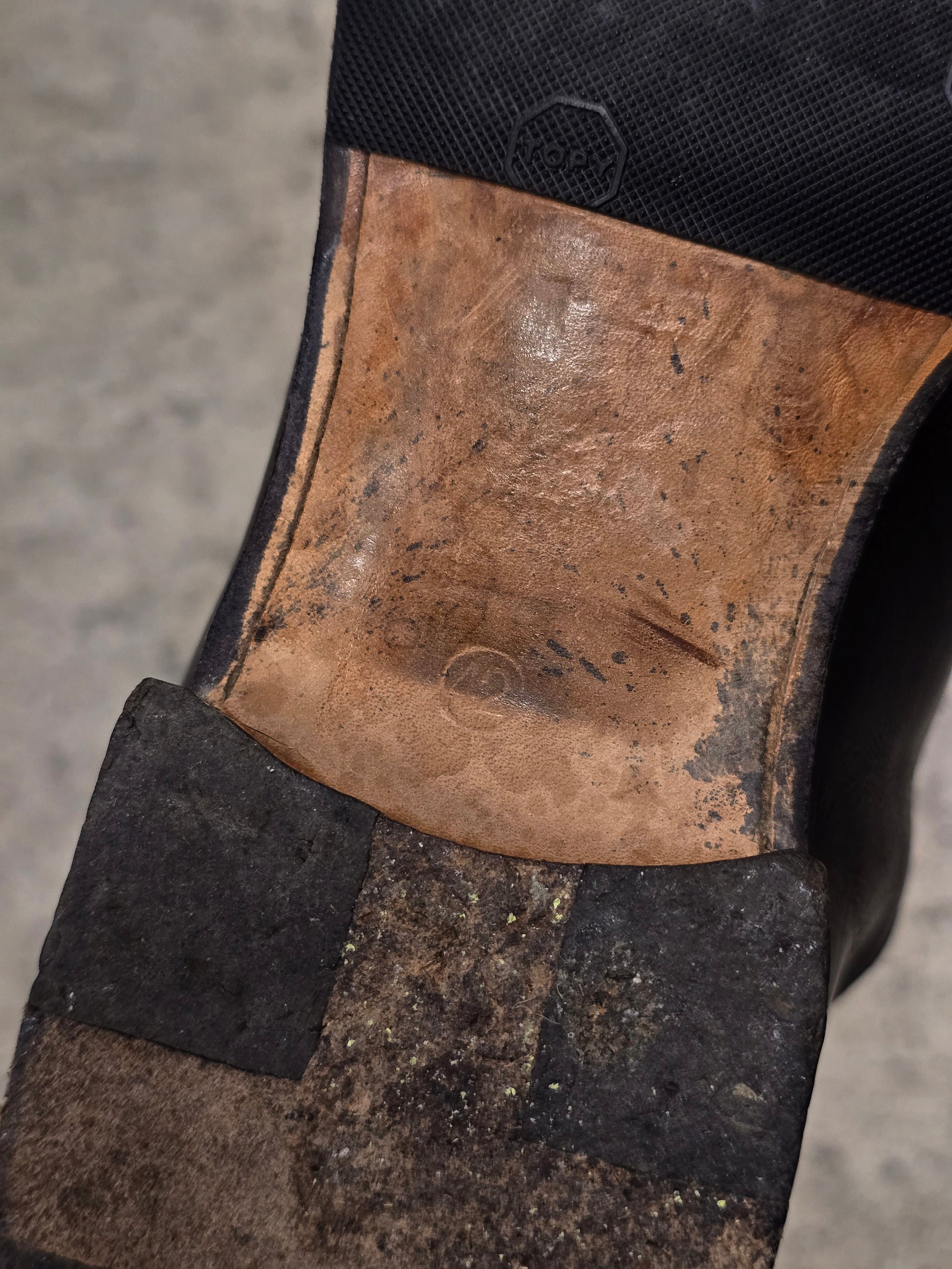 Close-up of a worn boot sole with visible dirt and scuff marks on a concrete surface.