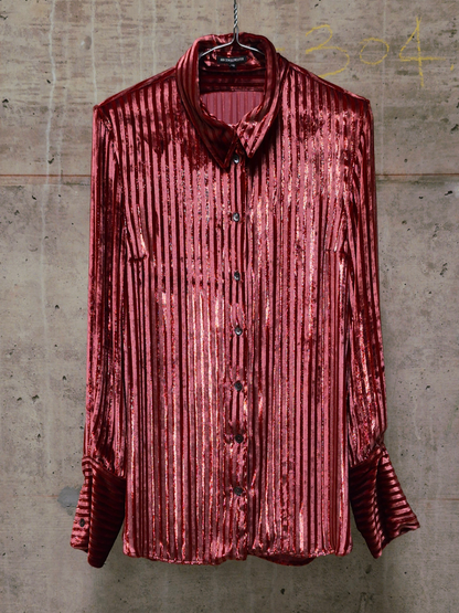 Red pleated shirt on a hanger against a textured wall.