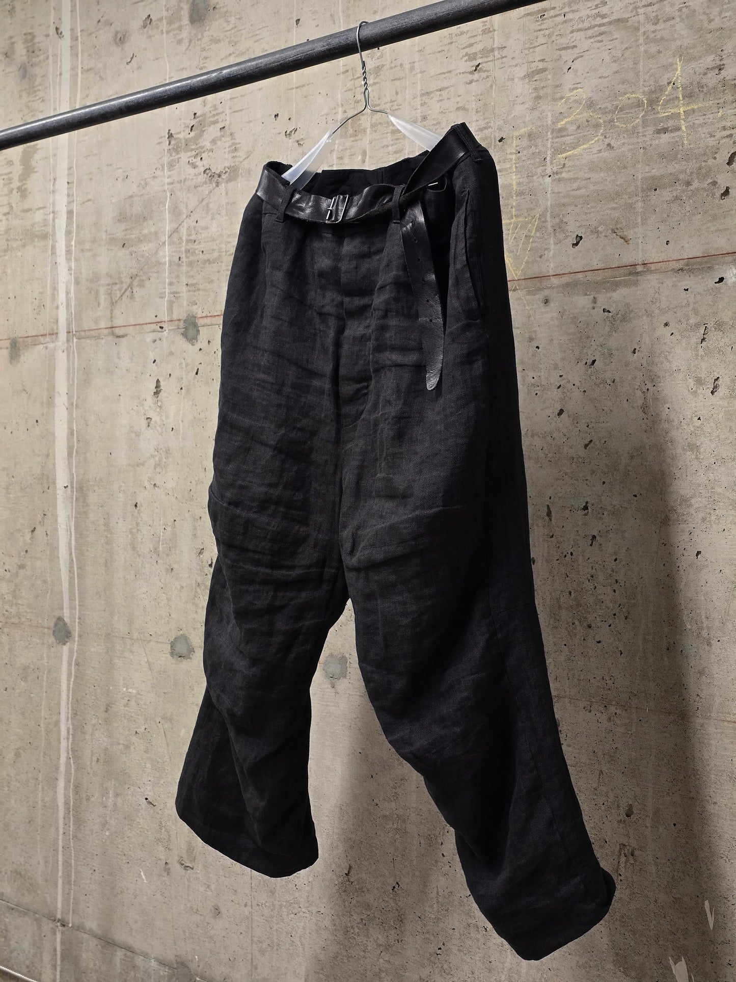 Black pants hanging on a hook against a concrete wall