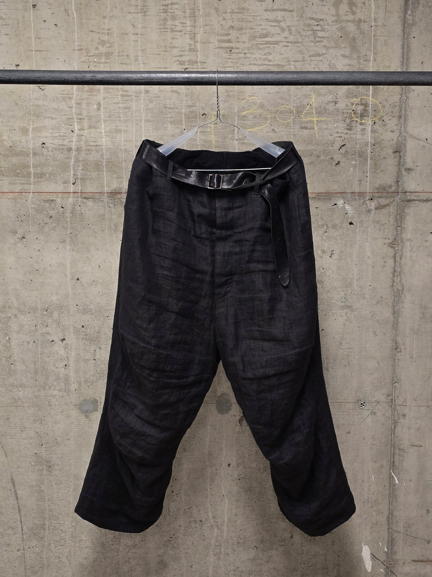 Black pants hanging on a rack against a concrete wall.