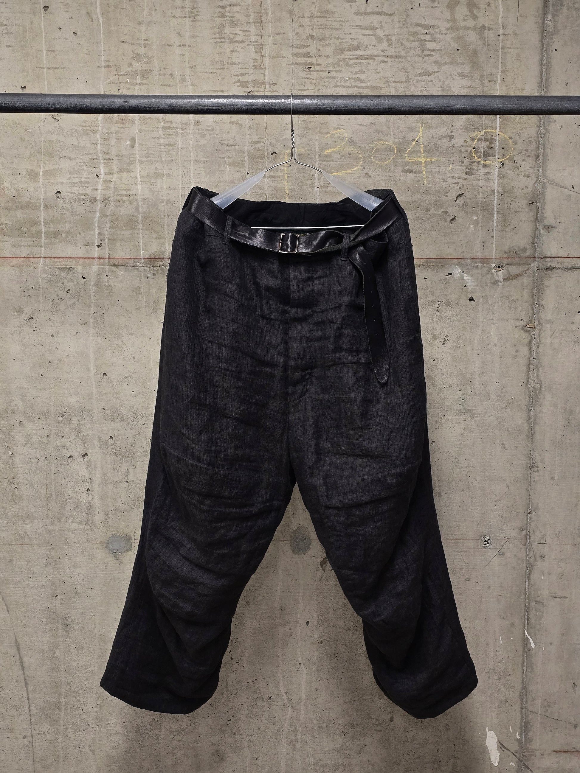 Black pants hanging on a rack against a concrete wall.
