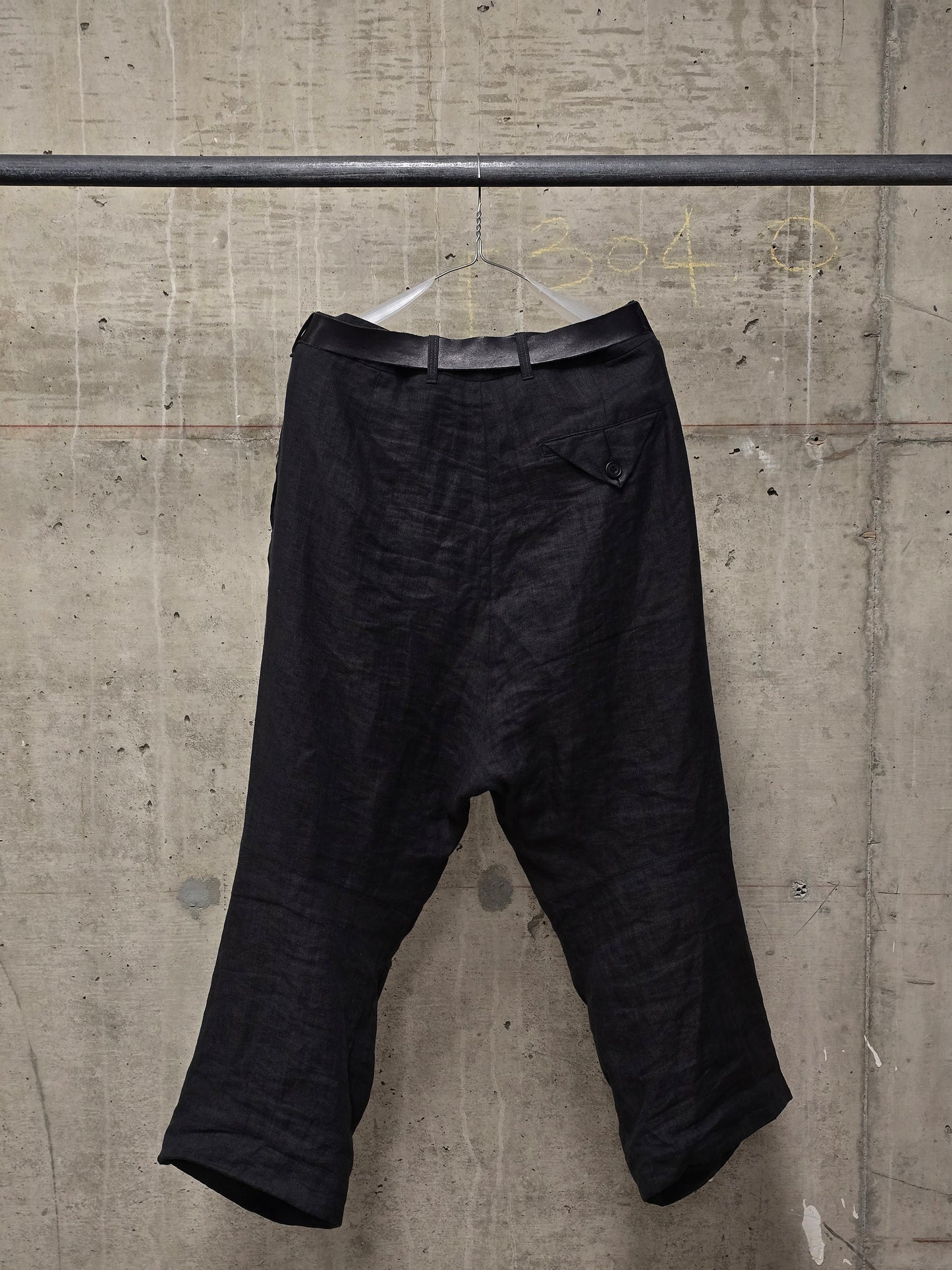 Black pants hanging on a metal rod against a concrete wall.