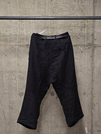 Black pants hanging on a metal rod against a concrete wall.